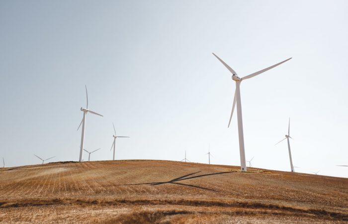 A landscape shot of white wind turbines on a peaceful dry grass field. Perfect for a renewable energy piece.